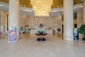 Un vestíbulo amplio con una recepción central, columnas imponentes y un candelabro moderno.