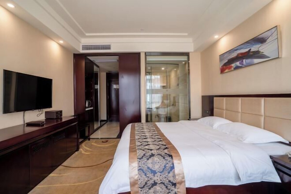 Habitación de hotel con una cama grande, televisión de pantalla plana, una consola de madera y un cuadro en la pared.