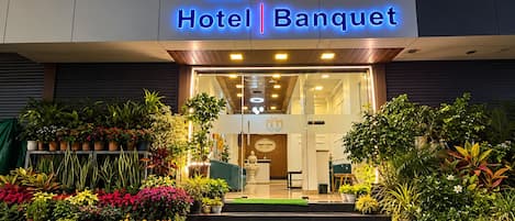 Der Eingang zum Mumbai House Hotel und zur Banketthalle, mit einem Schild über der Tür und verschiedenen Topfpflanzen davor.