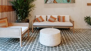 A room with a large tropical bird painting, a wooden slatted wall, a sofa with patterned cushions, a round ottoman, and a potted plant. - Isla Amara Resort (El Nido)