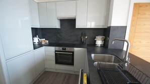 Una cocina compacta con armarios blancos, una encimera negra, un horno, un fregadero y un escurreplatos.