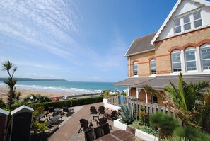 A beachfront property with a patio area, outdoor seating, and a view of the beach and ocean.