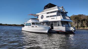 Eine weiße Yacht liegt in einer Marina festgemacht, mit einer mehrstöckigen Struktur, einer überdachten oberen Deck und blauem Himmel.