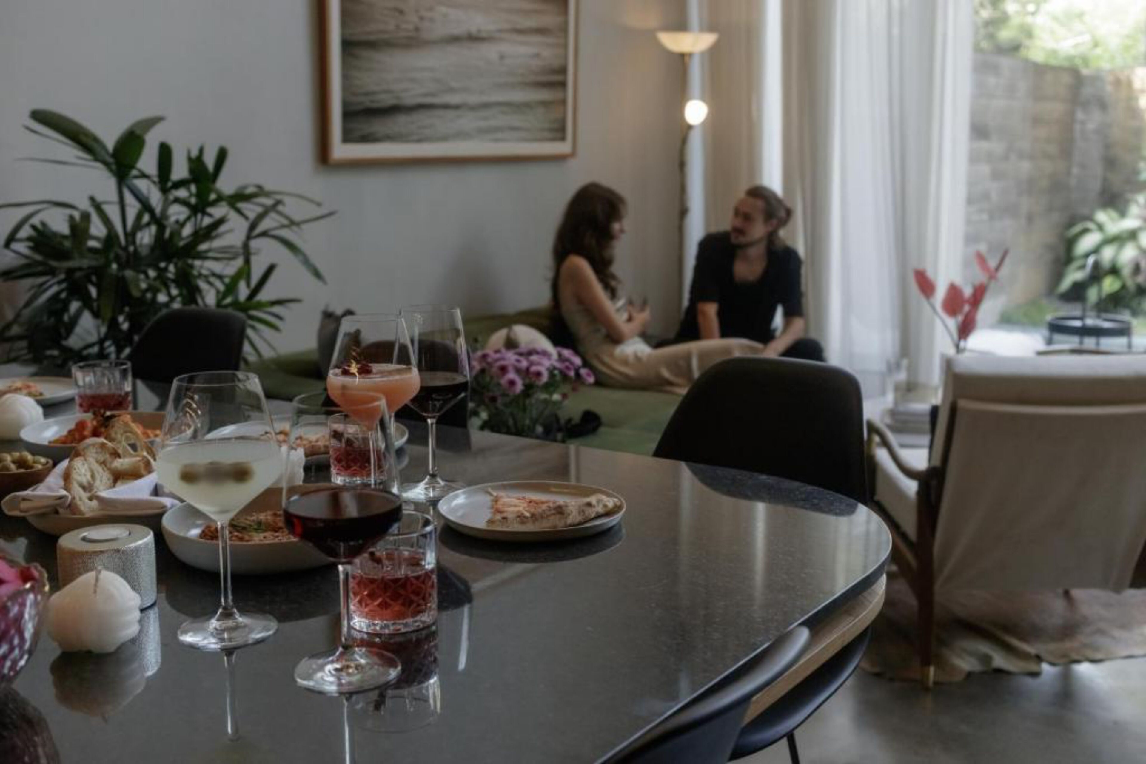 A dining table set with various dishes and drinks, surrounded by chairs and a sofa.