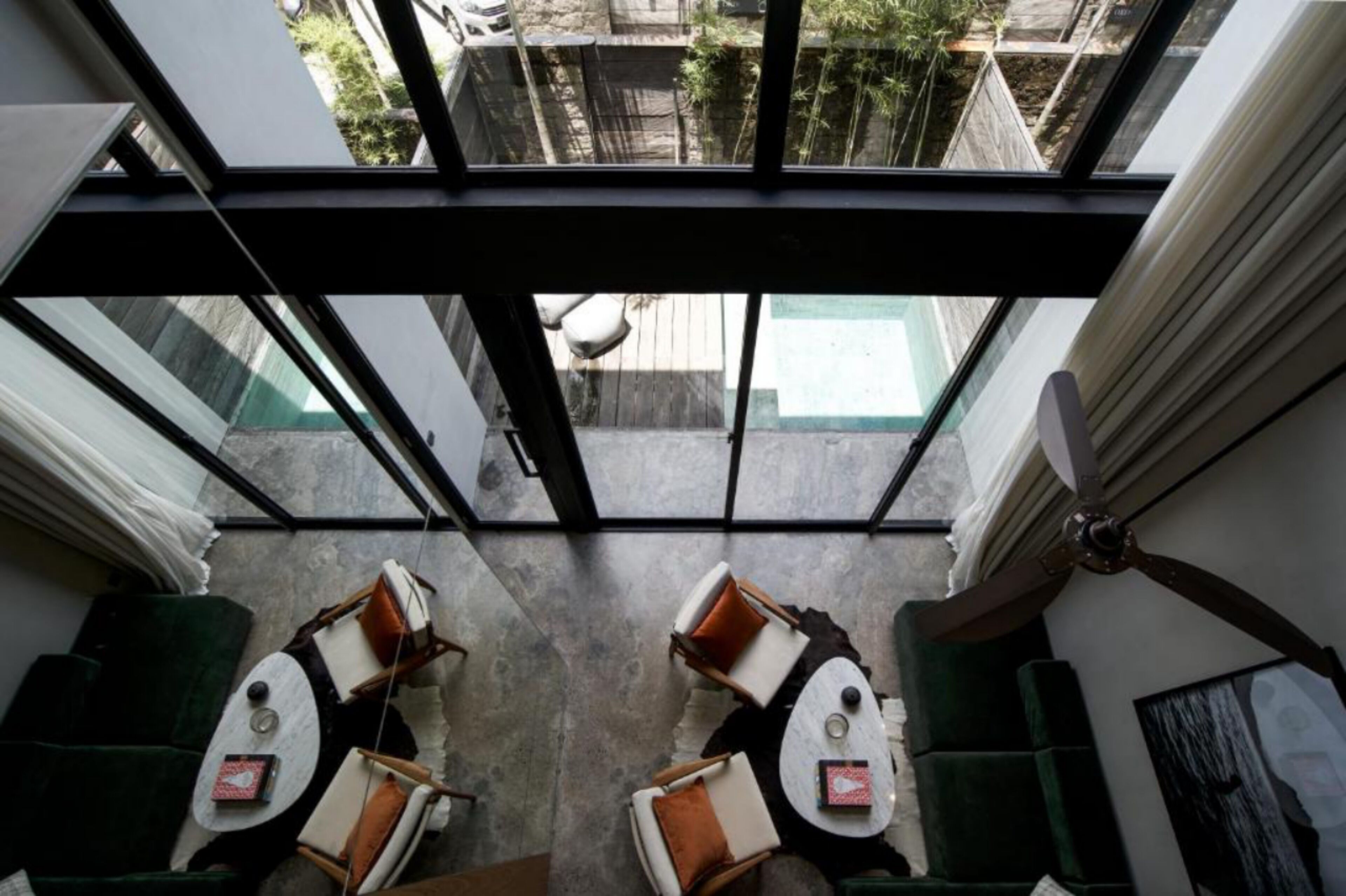 Un intérieur moderne avec un plafond en verre, deux coins salon dotés de coussins et une vue sur une cour intérieure.
