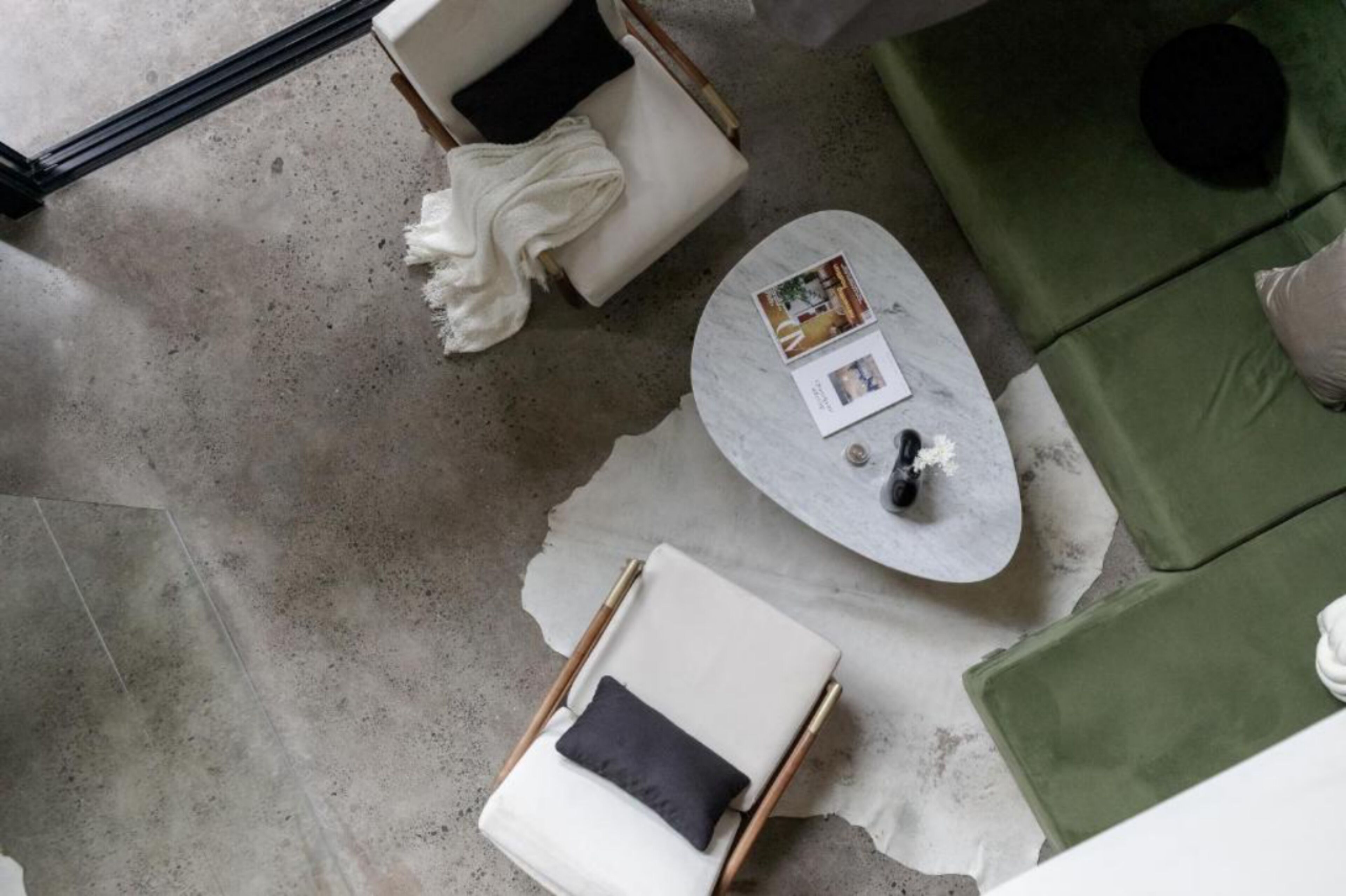 A modern living room with a white sofa, a green sofa, a round coffee table with magazines, and a white armchair with a throw blanket.