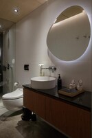 Un baño moderno con un espejo redondo, un lavabo blanco y un inodoro.