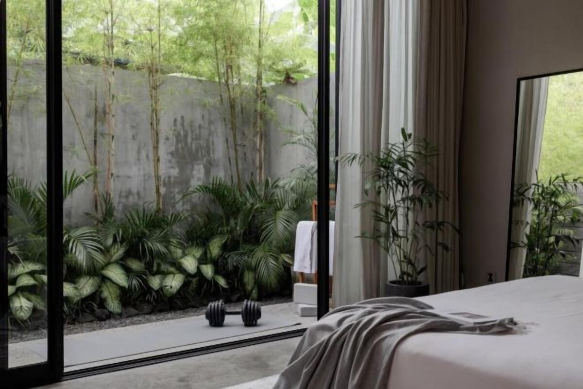Ein Schlafzimmer mit großem Fenster, einem Bett und Blick auf Grünfläche.
