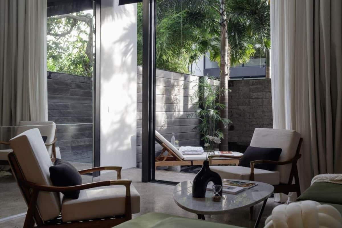 Een moderne woonkamer met een glazen deur die uitkomt op een balkon, ingericht met stoelen en een salontafel.