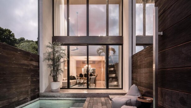 Une maison moderne dotée d’une grande porte vitrée donnant sur un espace repas, une petite piscine et une terrasse en bois.