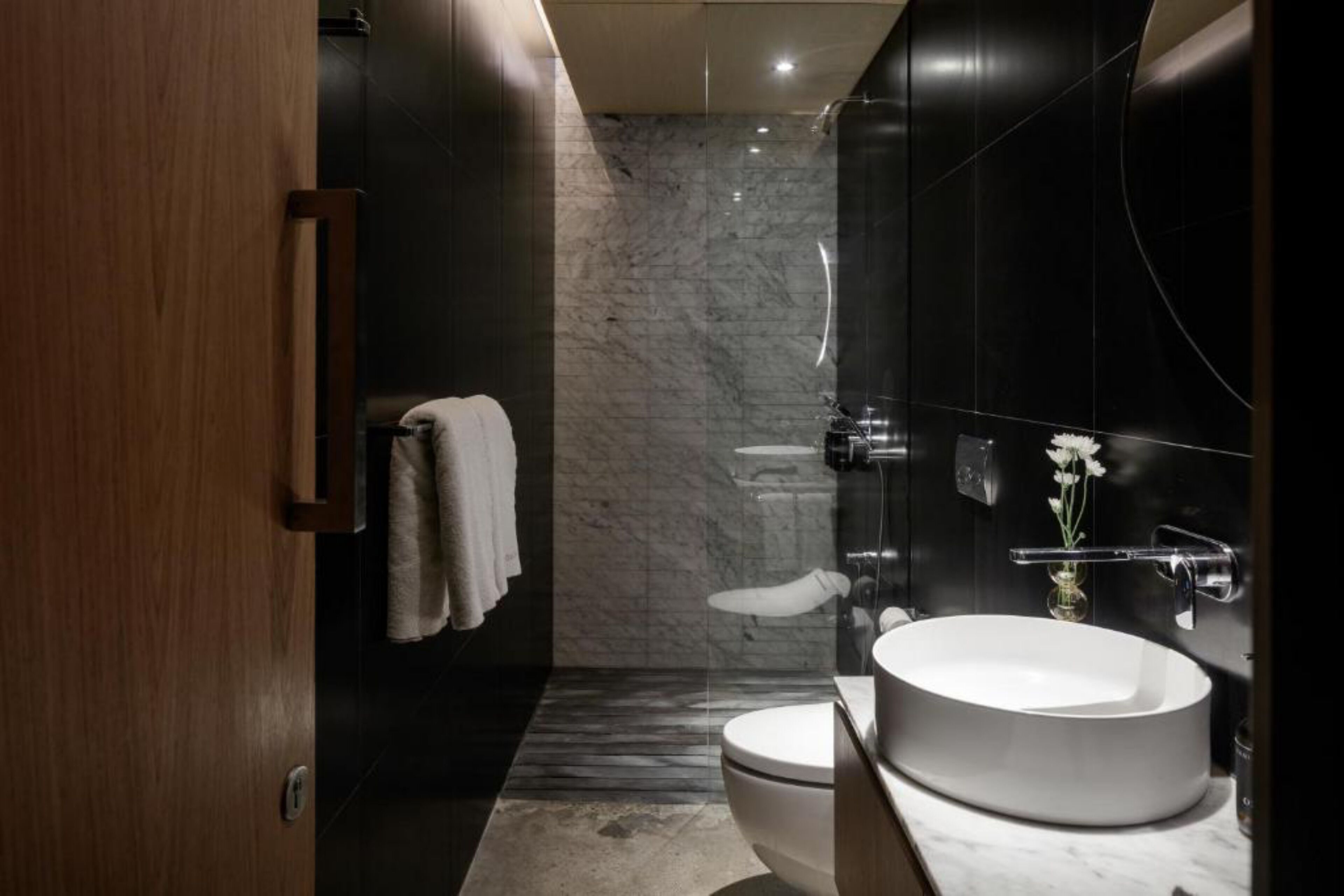 A modern bathroom with a marble wall, a round sink, and a toilet.