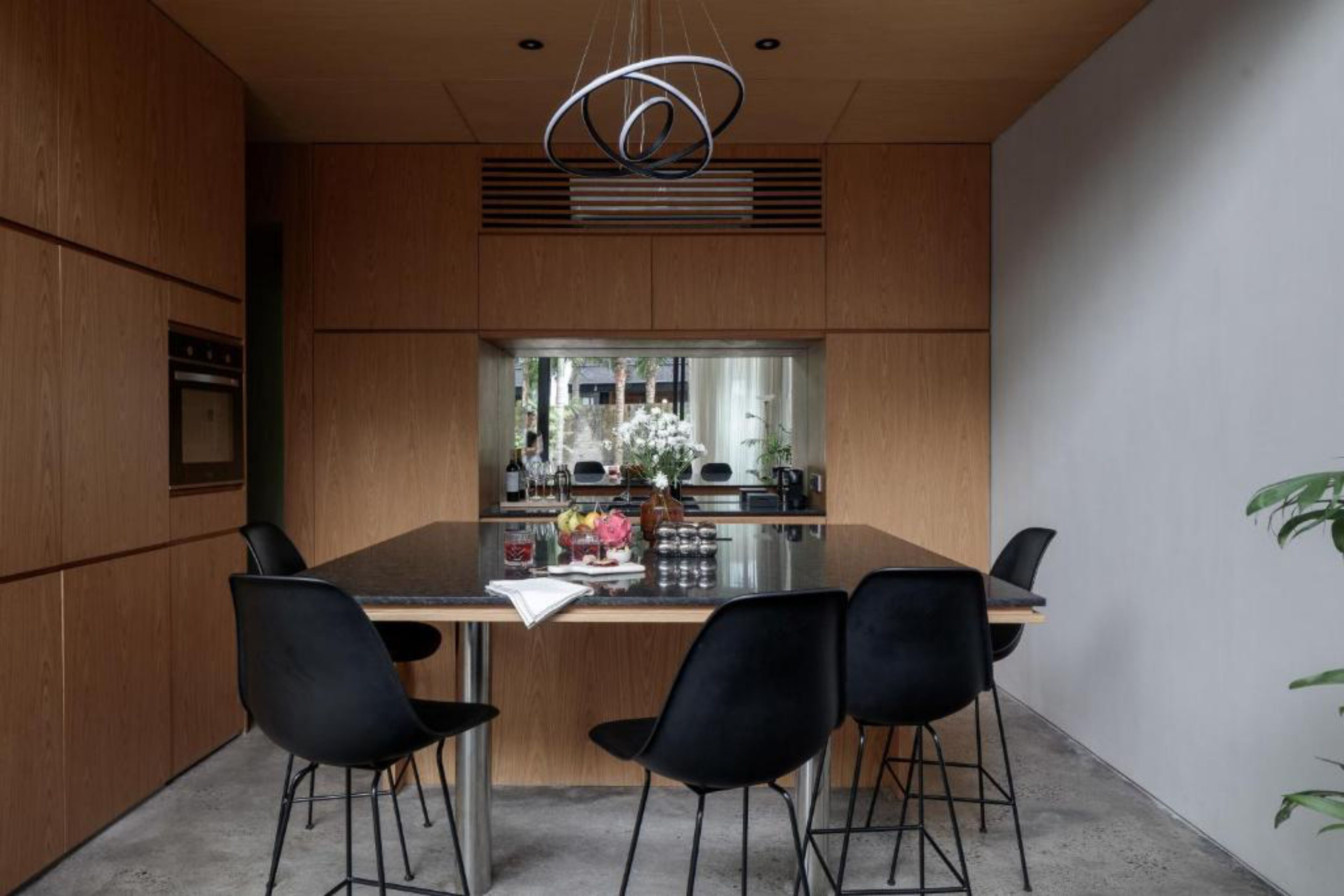 A modern kitchen with a central island, black chairs, and a stainless steel oven.