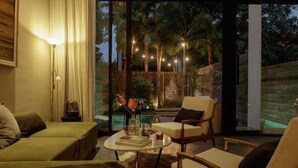 Un salon moderne avec un canapé, des fauteuils, une table basse et une vue sur une piscine et des arbres.