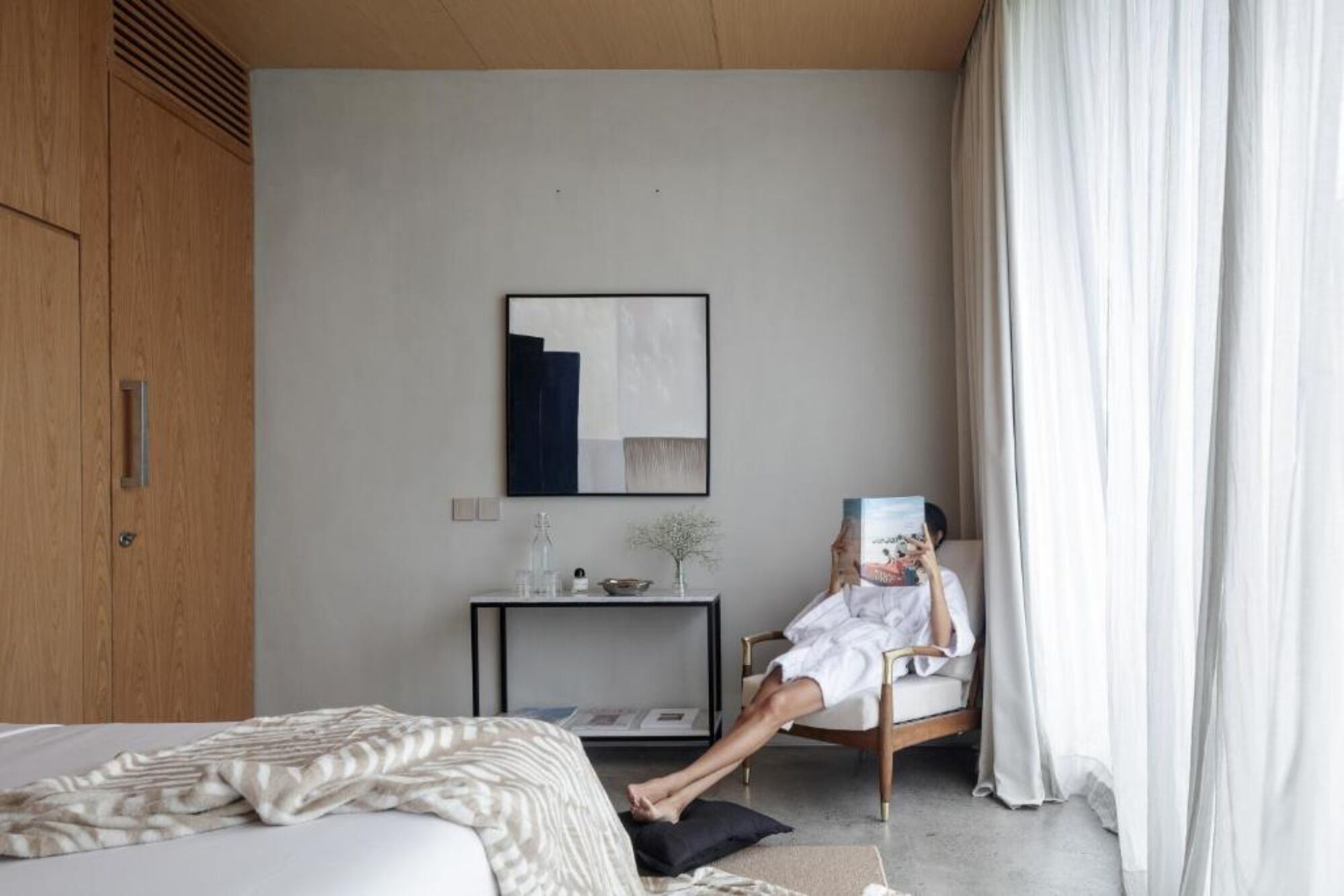 A modern bedroom with a bed, a chair, a small table, and a painting on the wall.