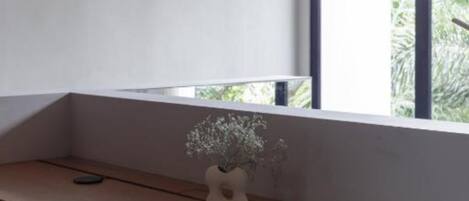 Quarto com escrivaninha de madeira, laptop, um vaso com flores e janela com vista para o verde.