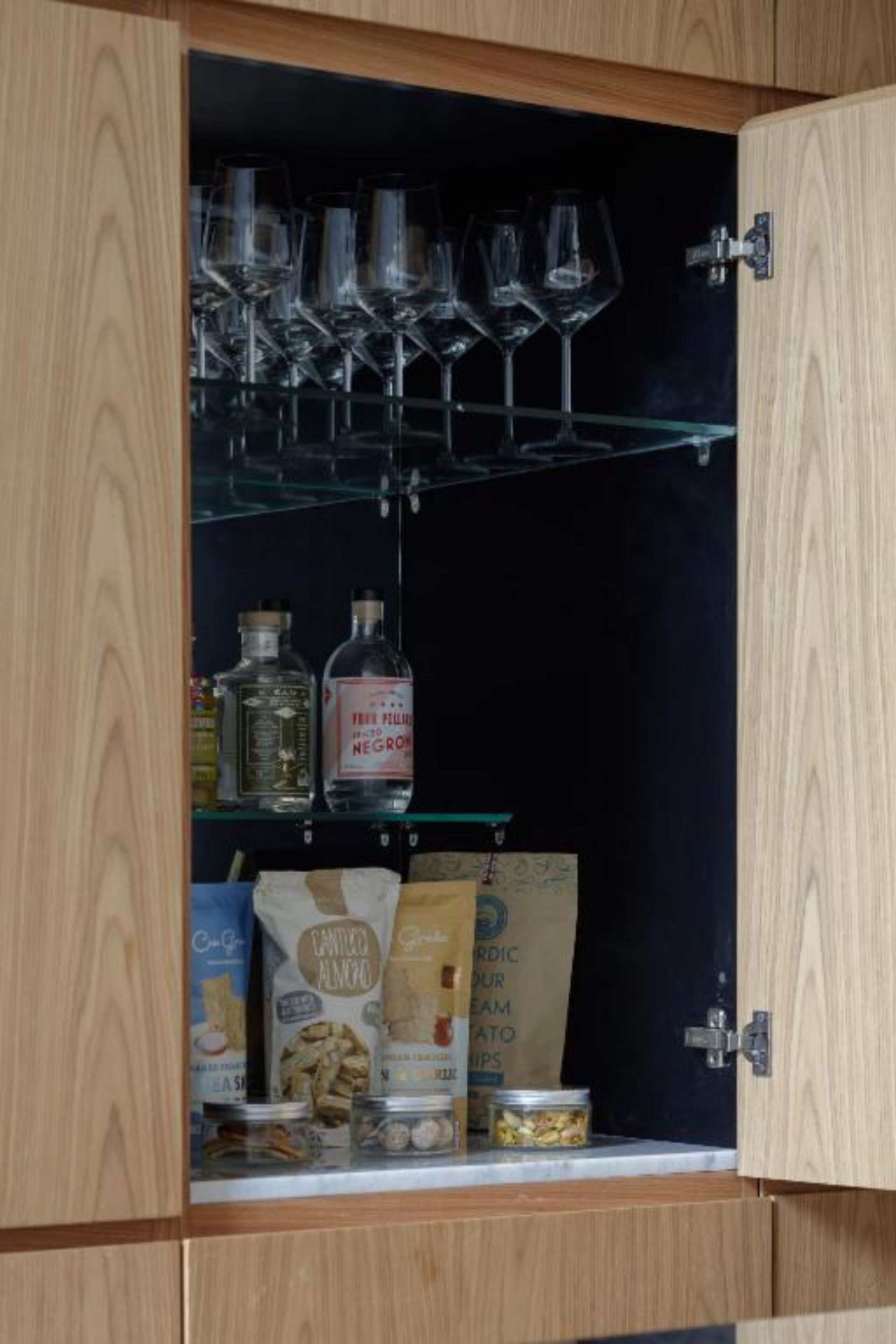 Un aparador de madera con estantes que contienen copas de vino, botellas y alimentos.