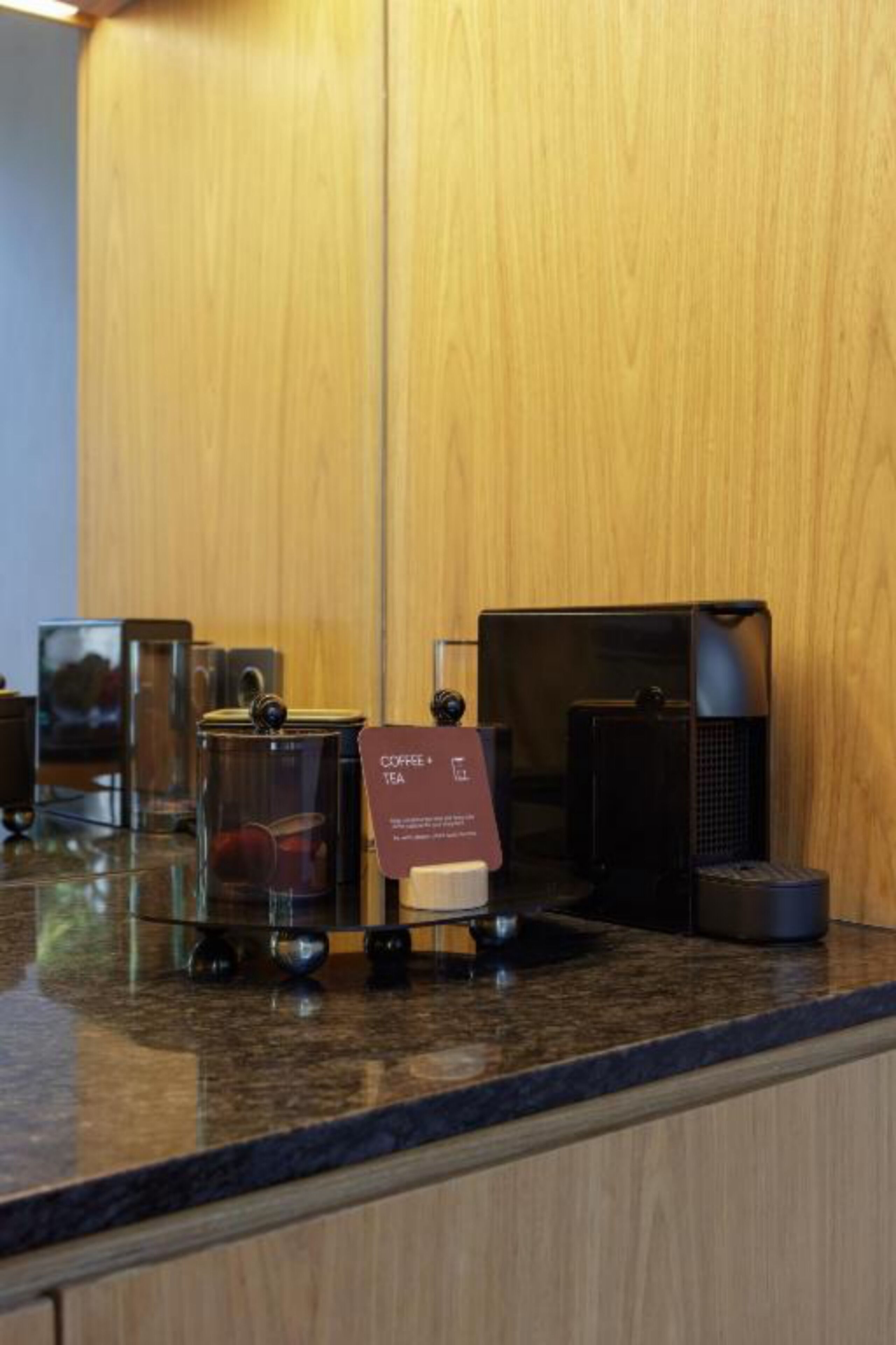 A coffee station with a sign indicating it is for coffee and tea, a coffee maker, and a glass container.