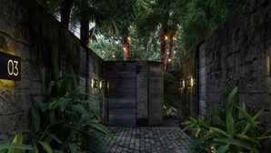 Une cour aux murs de pierre, dotée d’un chemin pavé, entourée d’une végétation luxuriante et illuminée de guirlandes lumineuses.
