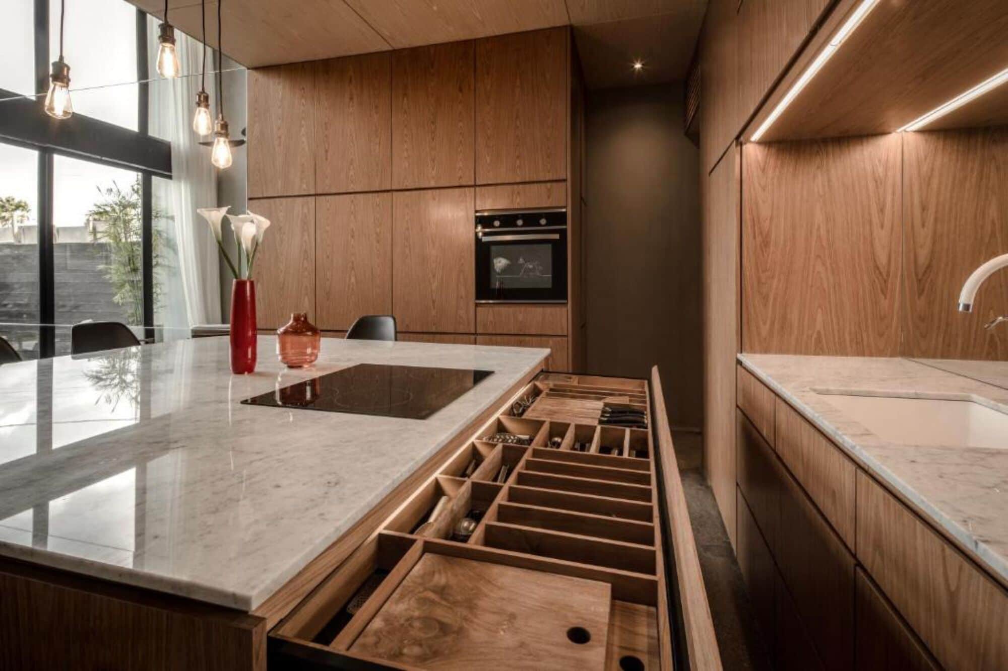 Une cuisine moderne avec des meubles en bois, un four encastré et un grand îlot central doté d’un évier et de tiroirs de rangement.