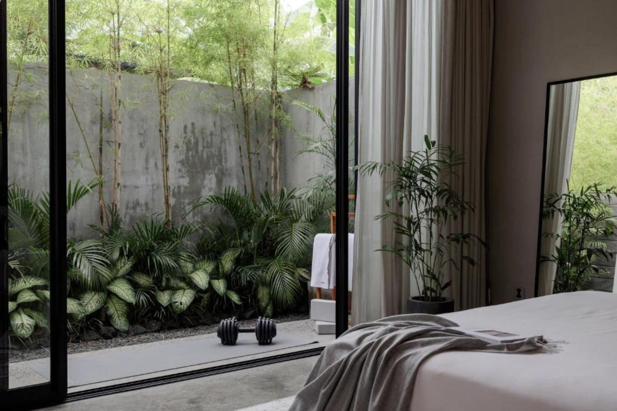 Une chambre avec une grande fenêtre, un lit et une vue sur un jardin agrémenté de bambous et d’autres plantes.