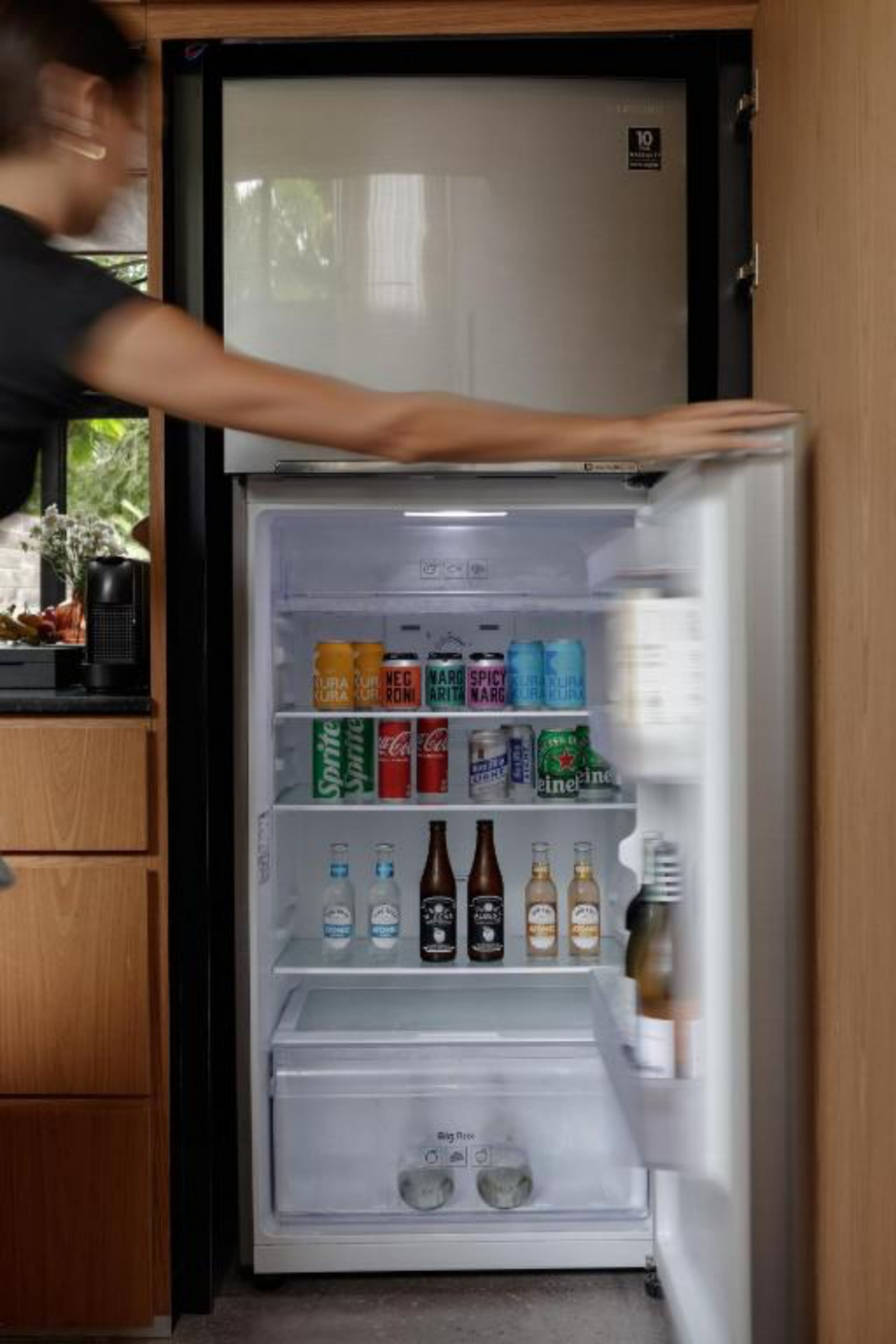 A refrigerator stocked with beverages and a person opening it.