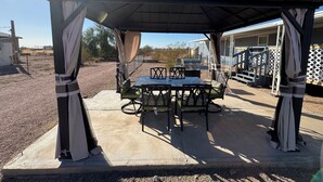 A covered patio area with a table and chairs, a grill, and a view of a residential area. - Newly updated home on spacious lot located outside of the city (Apache Junction)