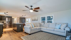 A modern kitchen with a built-in refrigerator and stove, a dining area with a table and chairs, a large beige sectional sofa, and a patterned rug. - Newly updated home on spacious lot located outside of the city (Apache Junction)