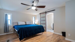 A bedroom with a bed, wooden flooring, a ceiling fan, and a sliding door leading to another room. - Newly updated home on spacious lot located outside of the city (Apache Junction)