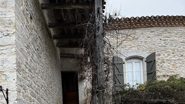 Un escalier en pierre mène à une porte en bois, qui est elle-même entourée de murs de pierre et de végétation.