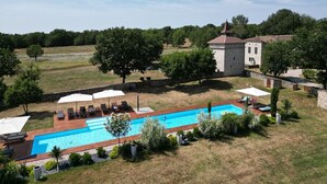Un espace piscine agrémenté de chaises longues et de parasols, entouré d’un mur de pierre et de verdure.