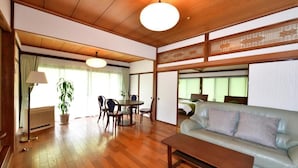 Uma sala de estar tradicional em estilo japonês, com piso de madeira, um sofá, uma mesa de jantar com cadeiras e um ventilador de teto.