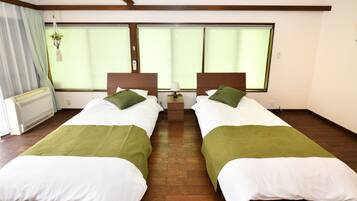 A twin room with two beds, each with a green pillow and white bedding, a bedside table, and a window with curtains.