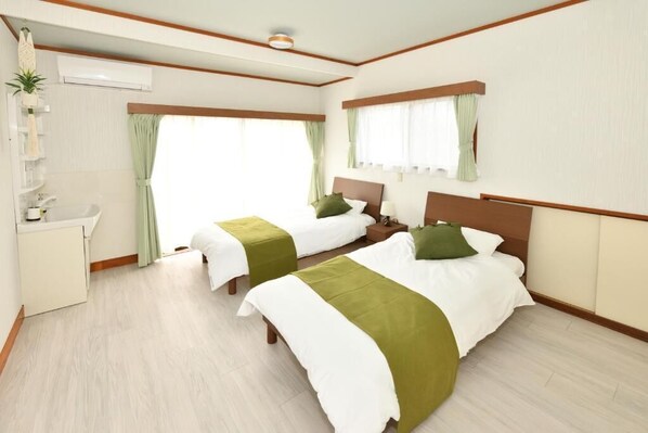 A hotel room with two beds, a small desk with a sink, and a window with curtains. - wasabi (Kamakura)