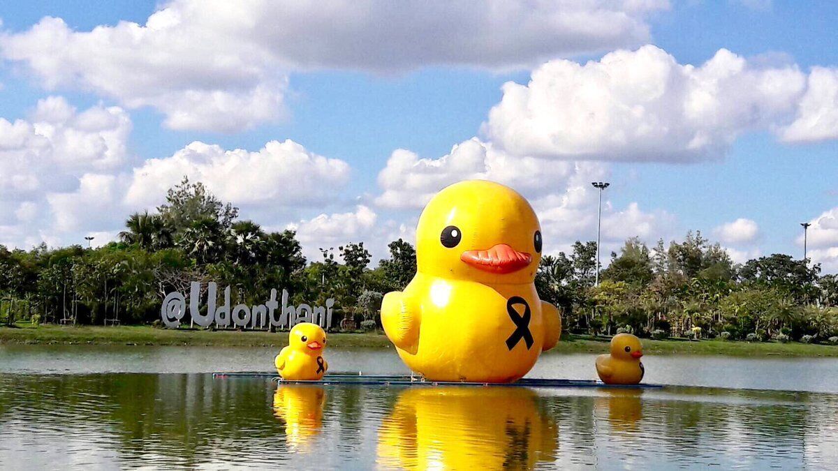 A large yellow duck sculpture with a ribbon symbol on a body of water, surrounded by greenery and trees.