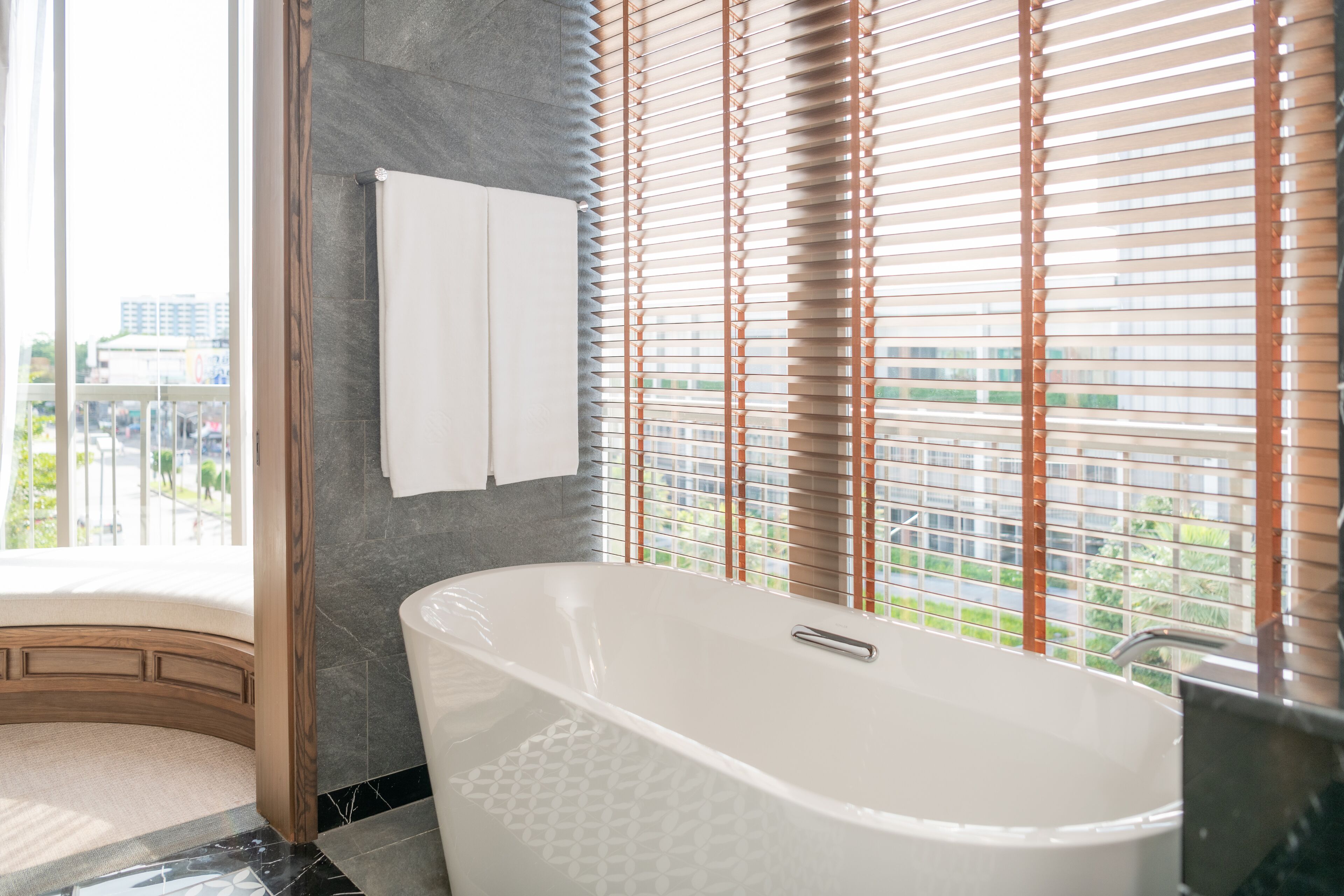 A modern bathroom with a freestanding bathtub, a towel rack, and a window with blinds.