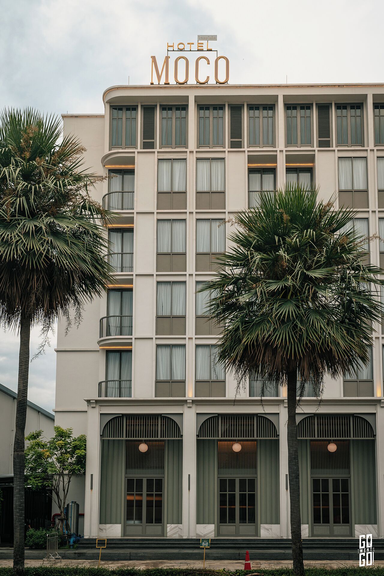 A hotel named "Hotel Moco" with a modern facade, multiple windows, and a prominent entrance with a large door and decorative elements.