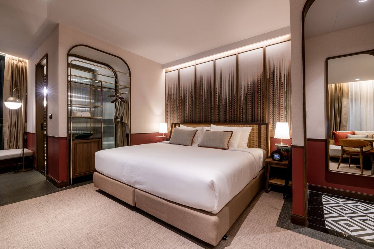 A spacious hotel room with a large bed, a walk-in closet, a sitting area with a chair, and a large mirror.