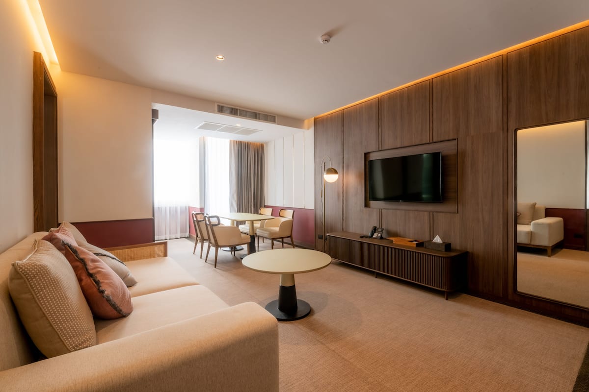 A modern hotel room with a sofa, a dining table, a TV, and a large mirror.