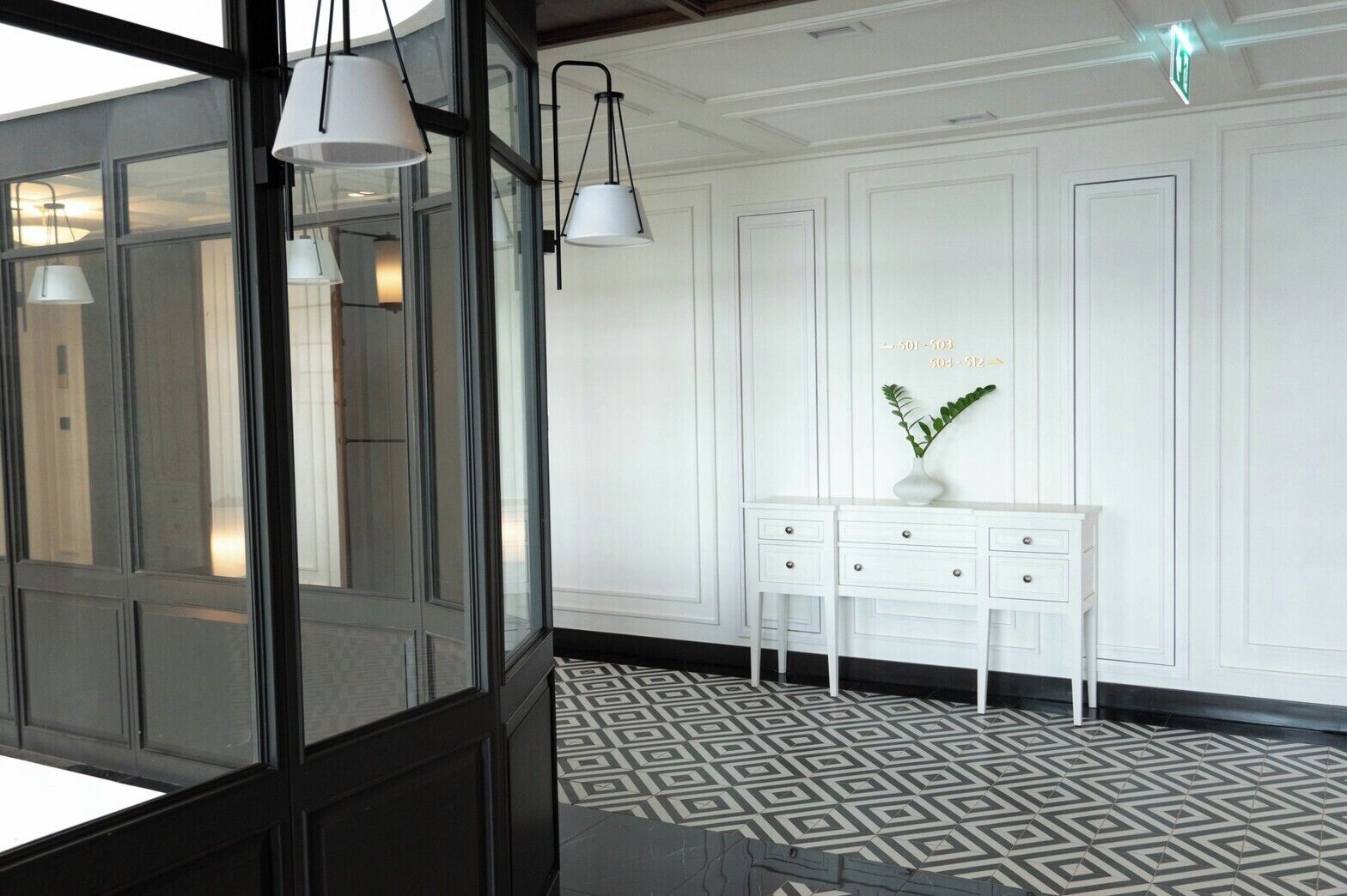 Un interior moderno con suelo de diseño geométrico, una consola blanca con cajones e iluminación colgante.