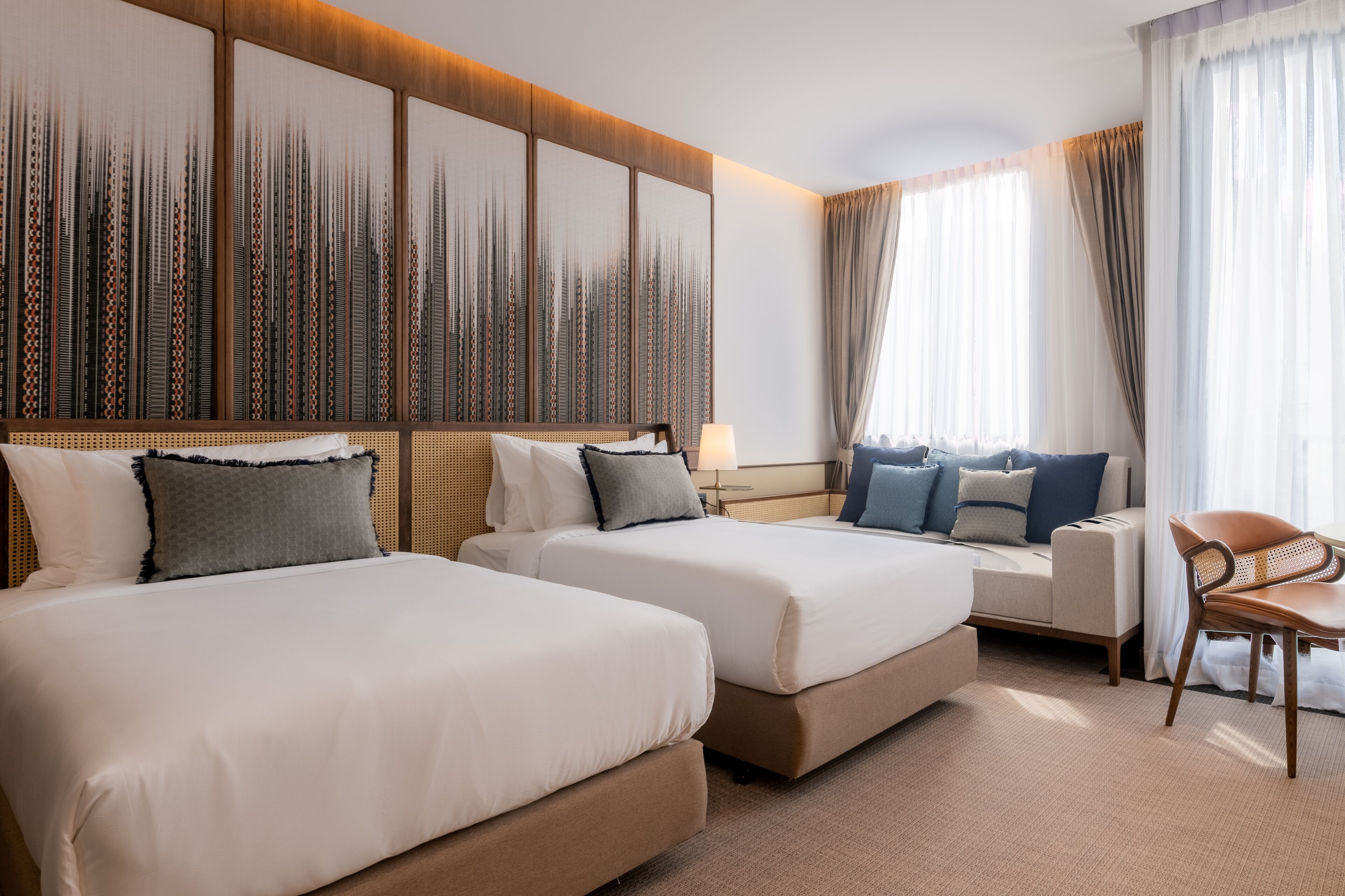 A hotel room with two beds, a sofa, a chair, and a large abstract wall art piece.