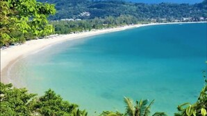A beach with clear turquoise water, a sandy shore, and lush greenery in the background. - Modern apt, full sea View,  4 min walk to kamala beach, pick up Airport service (Kamala)