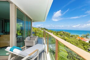 Ein Balkon mit Glasgeländer, der auf eine üppige Landschaft und den Ozean blickt.