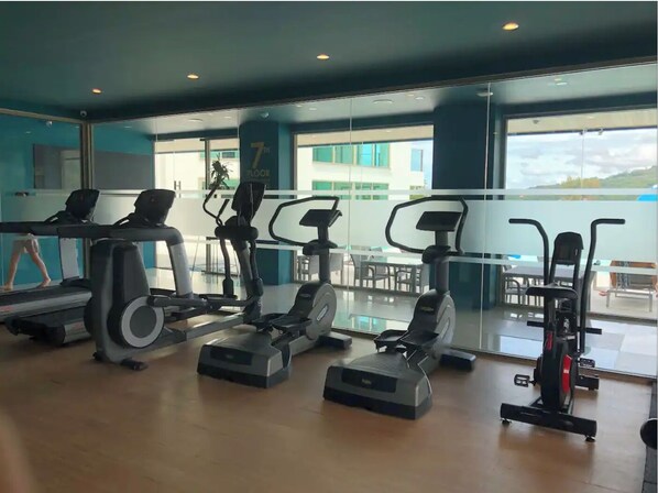 Ein Fitnessraum mit verschiedenen Trainingsgeräten, großen Fenstern und Blick ins Freie.