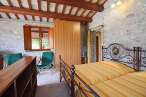 A bedroom with a wooden bed, green chairs, a wooden desk, and a stone wall.