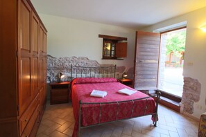 A bedroom with a bed, wooden wardrobe, stone wall, and a window with a view. - Belvilla by OYO Villa Fano (Isola di Fano)