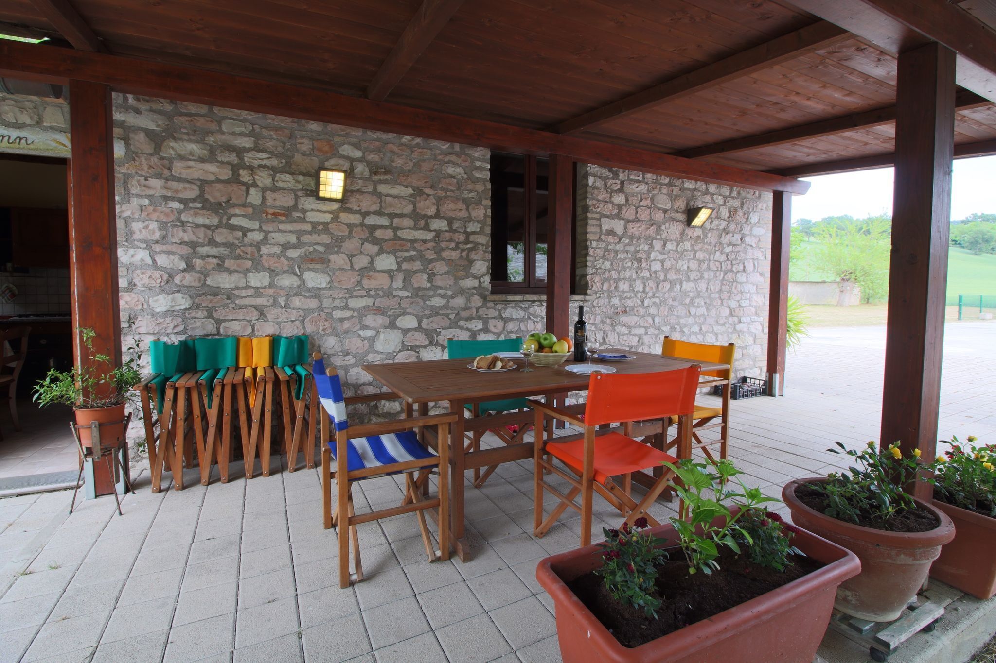 A covered patio with a stone wall, wooden furniture, and potted plants.