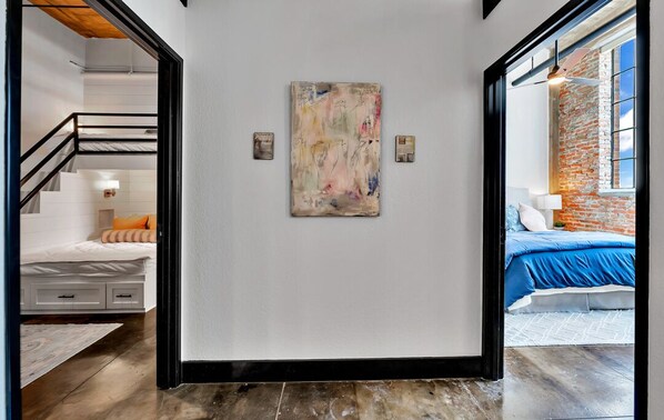 Un interior moderno con una escalera que lleva a un dormitorio, un cuadro abstracto grande en la pared y una pared de ladrillo con una ventana.