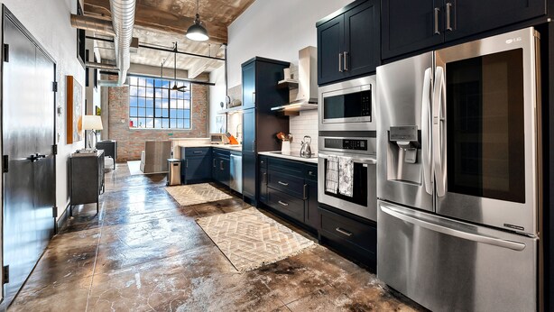 A modern kitchen with stainless steel appliances, dark cabinetry, and a visible brick wall. - Crusader Bear Hut- Downtown Waco- Steps To The Silos (Waco)