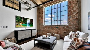 A modern living room with a large window, a fireplace, and a TV on the wall. - Crusader Bear Hut- Downtown Waco- Steps To The Silos (Waco)
