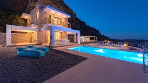 A modern house with a swimming pool, outdoor seating, and a view of the sea. - Villa in Rhodes with Infinity Pool (Kalythies)
